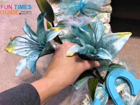 Adding blue artificial flowers to the baby shower diaper wreath.