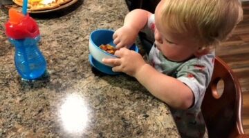 Toddler self feeding at the counter while sitting in his Keekaroo Right Height high chair